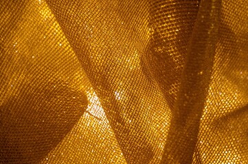 Close up of shimmering gold fabric with a textured net pattern and soft folds creating depth and light