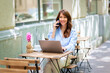 © sepy - Brunette haired woman sitting in an outdoor cafe and using smarpthone and computer laptop