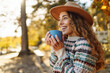 © maxbelchenko - Portrait of woman in hat with cup of hot tea from thermos sitting on bench in autumn park. Beautiful female traveler enjoying hot drink on sunny day. Rest and relaxation concept.