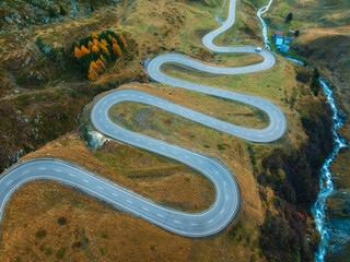 Wall Mural - aerial view of winding mountain road, river in alpine valley at sunset in autumn. top drone view of 