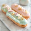 Three glossy eclairs, glazed in pastel shades, boast delicate fondant flowers and edible gold accents. They sit invitingly on a marble platter against a gentle, blurred backdrop