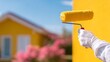 © Margarita Ratatosk - Hand of a man in white glove painting wall with yellow paint roller. Home renovation work concept for building improvement.