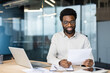 © Liubomir - Smiling businessman reviewing documents at desk in modern office setting
