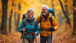 © Viktor - Energetic older couple hikes through vibrant autumn forest. Smiling seniors wear hiking gear, use walking sticks. Companions enjoy fall foliage scenery, practicing outdoor fitness, healthy lifestyle.