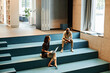 © TrueFrame Collective - Horizontal high angle view long shot of young African American man and Caucasian woman sitting on stair bench in modern library using Internet, drinking coffee and chatting