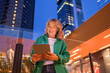 © Westend61 - Smiling woman using tablet in urban street during evening