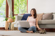© interstid - Happy Asian woman smile and have fun playing with cat while using laptop for working or online shopping at home in living room