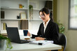 © Prathankarnpap - Smiling businesswoman working on laptop while holding a coffee mug in modern office