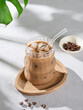 © Kufotos - Ice latte coffee in a glass with milk and straw on a wooden plate on light background with coffee beans