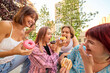 © Lustre Art Group  - Group of young friends laughing and sharing donuts outdoors in sunny urban park. Concept of friendship, joy, indulgence, street food, summer leisure, and positive emotions.