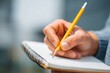 © Vitalii Shkurko - A student is holding a sharpened pencil and a blank notebook, preparing to take notes. The focus is on their intent to capture important information during study time