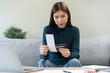 © KMPZZZ - Stressed asian young business woman, employee calculate expenses of monthly, hand holding bills, receipt and credit card to payment on table at home. Financial, finance of banking concept.