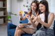 © Apichat - Two women sitting on a couch, one holding a credit card