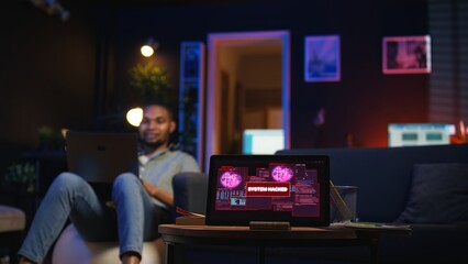 Black IT professional in loft working on cybersecurity with gadgets, tackling hacking attempts, encryption and cyber defense. Screen shows security breach warning, data security risks. Camera A.