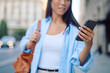 © we.bond.creations - Asian businesswoman walking through an urban street, holding a smartphone and checking messages against a blurred city backdrop