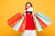 © ViDi Studio - Young woman wear red casual clothes hold paper package bags after shopping hold gift coupon voucher card for store wink isolated on plain orange yellow background. Black Friday sale buy day concept.
