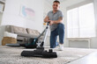 © New Africa - Man cleaning carpet with vacuum cleaner at home, low angle view
