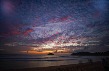 Wall Mural - Island Glow at Kata Beach Phuket. The last rays of sunshine illuminate the clouds with vibrant colors, blending seamlessly with the turquoise waters, a perfect moment of peace and wonder.