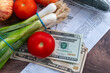 © Ming - A US cost of living concept with a pile of US Dollar bills, grocery receipts and some fruit and vegetable groceries on a table.