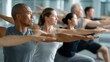 © dee-nesia - Diverse group of adults practicing yoga, arms outstretched in a synchronized pose, during a fitness class.
