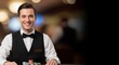 © Dmitry - Happy caucasian man dressed as a croupier at a casino table. Professional male dealer with poker chips. Entertainment industry backdrop.