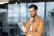 © Liubomir - Man using a tablet in a modern office space with a thoughtful expression