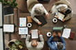 © pressmaster - Top view showing group of middle aged multiethnic business professionals working together at conference table, analyzing documents, using laptop, writing notes, drinking coffee during meeting