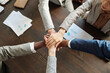 © pressmaster - Diverse group of young adult and middle aged men and women stacking hands in teamwork gesture on wooden table, showing multiethnic collaboration during business meeting from top view