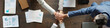 © pressmaster - Multiethnic group of young adult and middle aged men and women stacking hands in teamwork gesture on wooden table