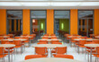 © Graphic Fizz - Bright orange chairs and light wood tables fill a modern cafeteria dining area dining hall