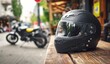© andyaziz6 - Close-up of a black motorcycle helmet resting on a wooden with a blurred urban street background featuring motorcycles and greenery