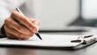 © Arpatsara - A close-up of a hand holding a pen, poised to write on a sheet of paper in a professional setting.