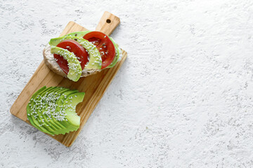 Wall Mural - Wooden board of tasty bruschetta with avocado and tomatoes on light background