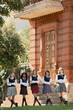 © master1305 - Teenage girls in colorful plaid skirts standing outside historic school with strong mood. Concept of YA culture, book covers, teen series promotion and modern group identity.