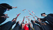 © Довидович Михаил - Group of students wearing graduation gowns and caps, joyfully throwing diplomas into the air against a clear blue sky, celebrating their academic achievement