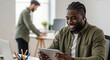 © Ismatara - A young african businessman is working on a tablet in the office, collaborating with his team on a project and planning a strategy