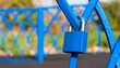 © jakiyo - A vibrant blue padlock secures a metal fence in an outdoor setting.