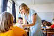 © Zoran Zeremski - Smiling teacher assisting young girl with assignment at school desk in classroom.