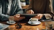 © Felippe Lopes - Two people looking at tablet in cafe with coffee and water glasses on wooden table The image is taken in a warm tone
