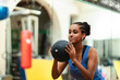© Studio Marmellata - A young woman with braided hair holds a medicine ball, ready for exercise in a gym. She is focused on her fitness routine, embodying strength and healthy living.