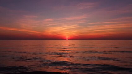 Wall Mural - Vibrant Sunset Over Ocean - A breathtaking timelapse captures the serene beauty of a sunset over the ocean. Vibrant hues of orange, red, and purple paint the sky and reflect on the calm water.