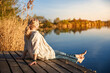 © encierro - Woman sitting and relaxing barefoot on wooden pier by still lake during golden hour of indian summer