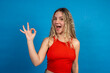 © EDUARDOIVAN - Enthusiastic young woman showing ok sign with blue background