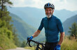 © miss irine - Happy 60-year-old man smiles wearing cycling gear, helmet posing with sleek road bike. Biker stands on scenic path with blurred mountain range background. Represents active lifestyle, outdoor