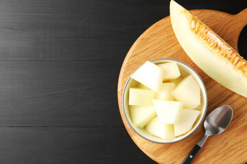 Wall Mural - Cut ripe melon in bowl on black wooden table, flat lay. Space for text