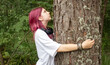 © Olena Rudo - Young woman with pink hair hugging a tree in a forest, showing love for nature