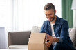 © Prostock-studio - Happy middle-aged man unpacking delivery box, sitting on couch by tea table, home interior. Satisfied customer cheerful man opening package, ordering clothes or gadgets on Internet, copy space