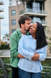 © CarlosBarquero - An interracial millennial couple shares a tender moment as the man kisses the woman on the cheek, symbolizing romance, love, affection, and emotional connection outdoors.