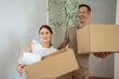 © Dexon Dee - Smiling couple carrying cardboard boxes with household items while moving into new home.