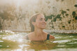 © Reuben - A woman is smiling while swimming in a pool. The water is clear and calm, and the sun is shining brightly overhead. The woman is enjoying her time in the water